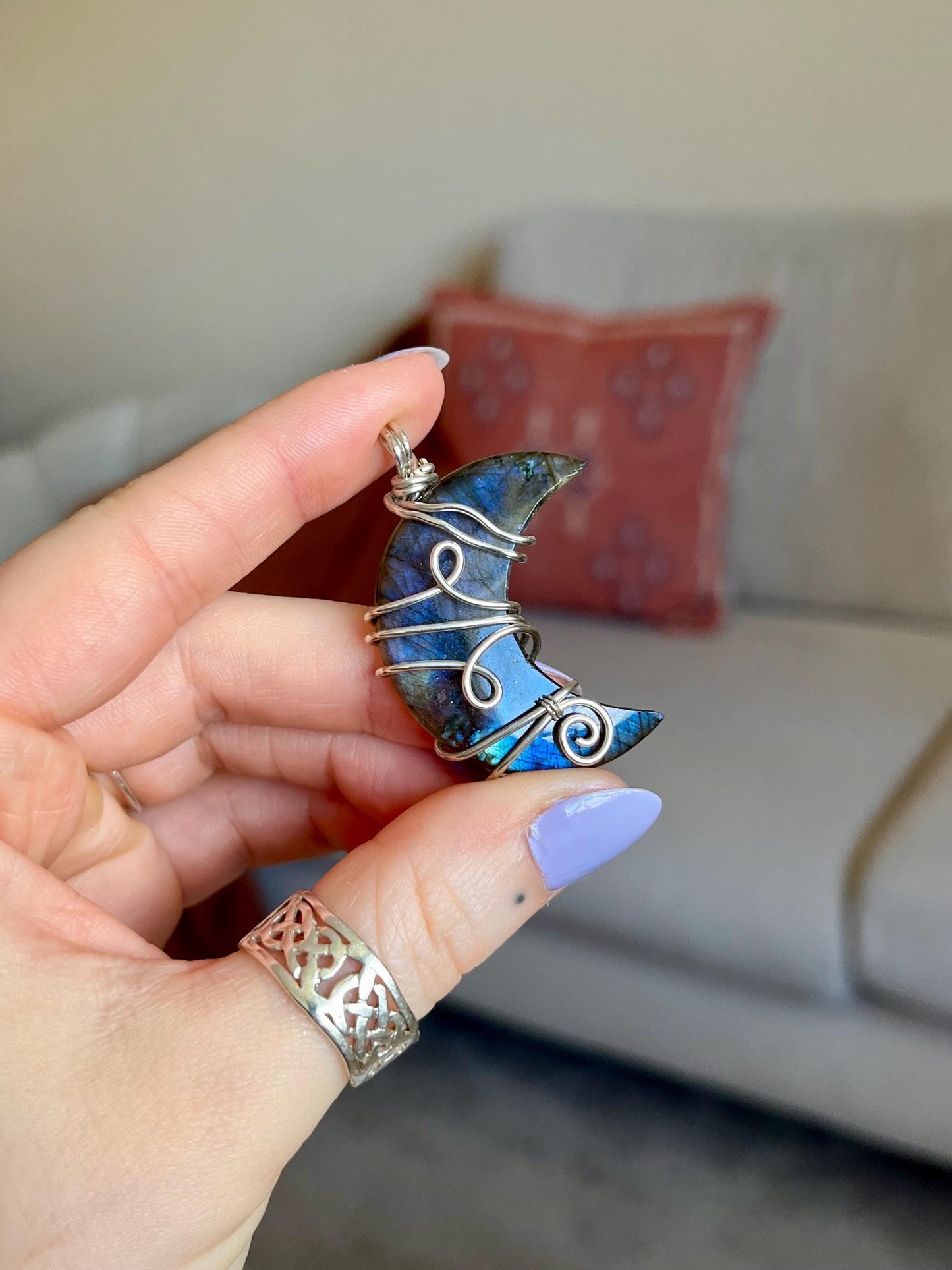 Hand holding a blue Labradorite moon-shaped pendant with wire wrapping, blurred background