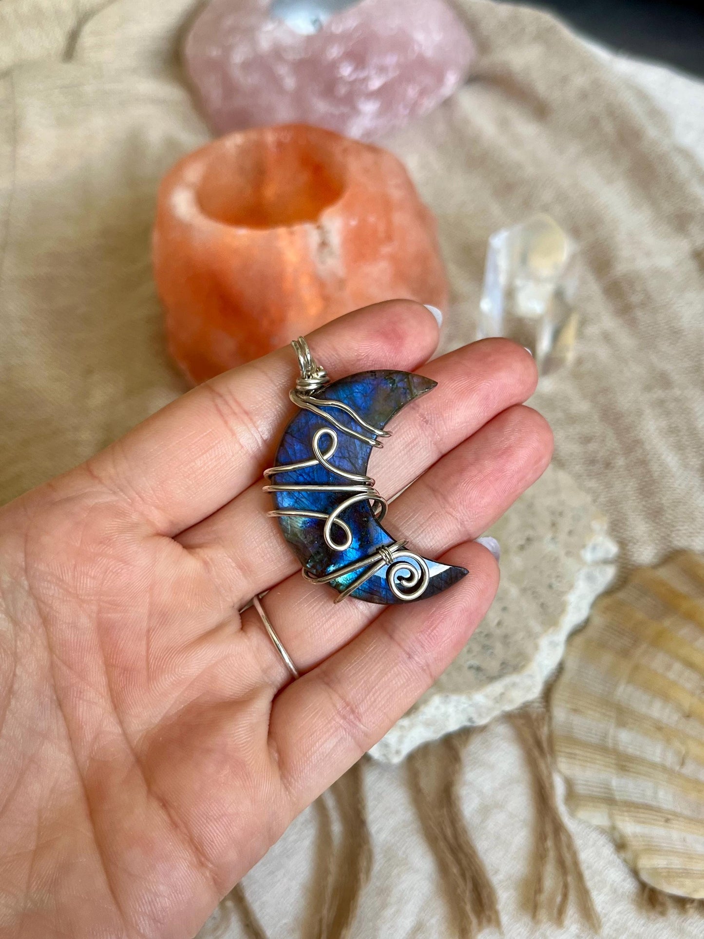 Hand holding a blue Labradorite stone pendant with wire wrapping against a natural stone background