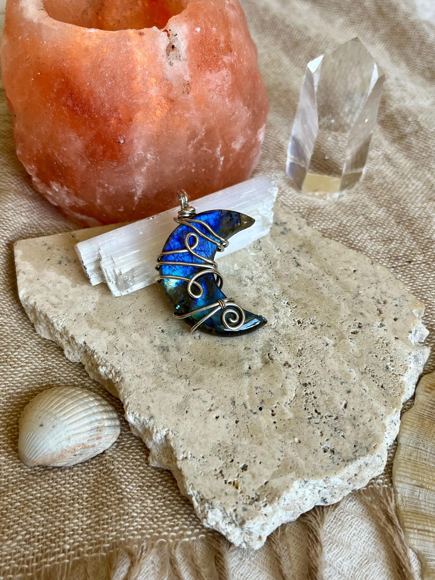 Blue crescent moon pendant on a stone surface with a salt lamp and crystal in the background