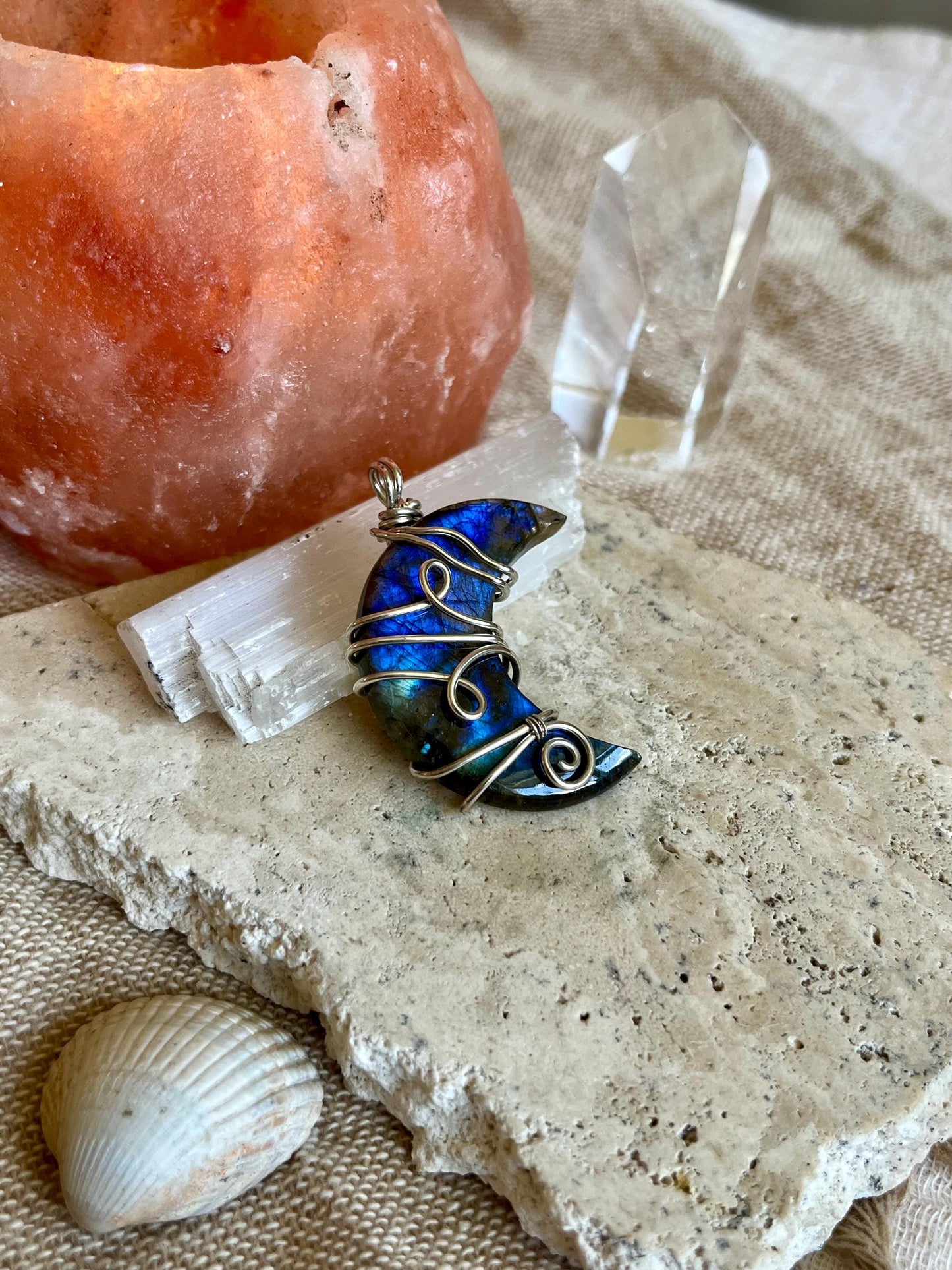 Blue wire-wrapped pendant on a stone surface with crystals and a shell.