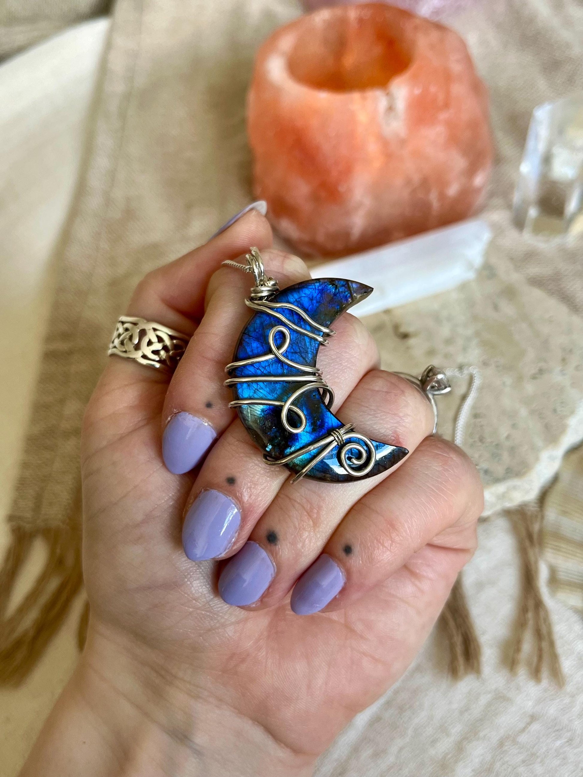 Hand holding a blue Labradorite and silver crescent moon pendant with a blurred background