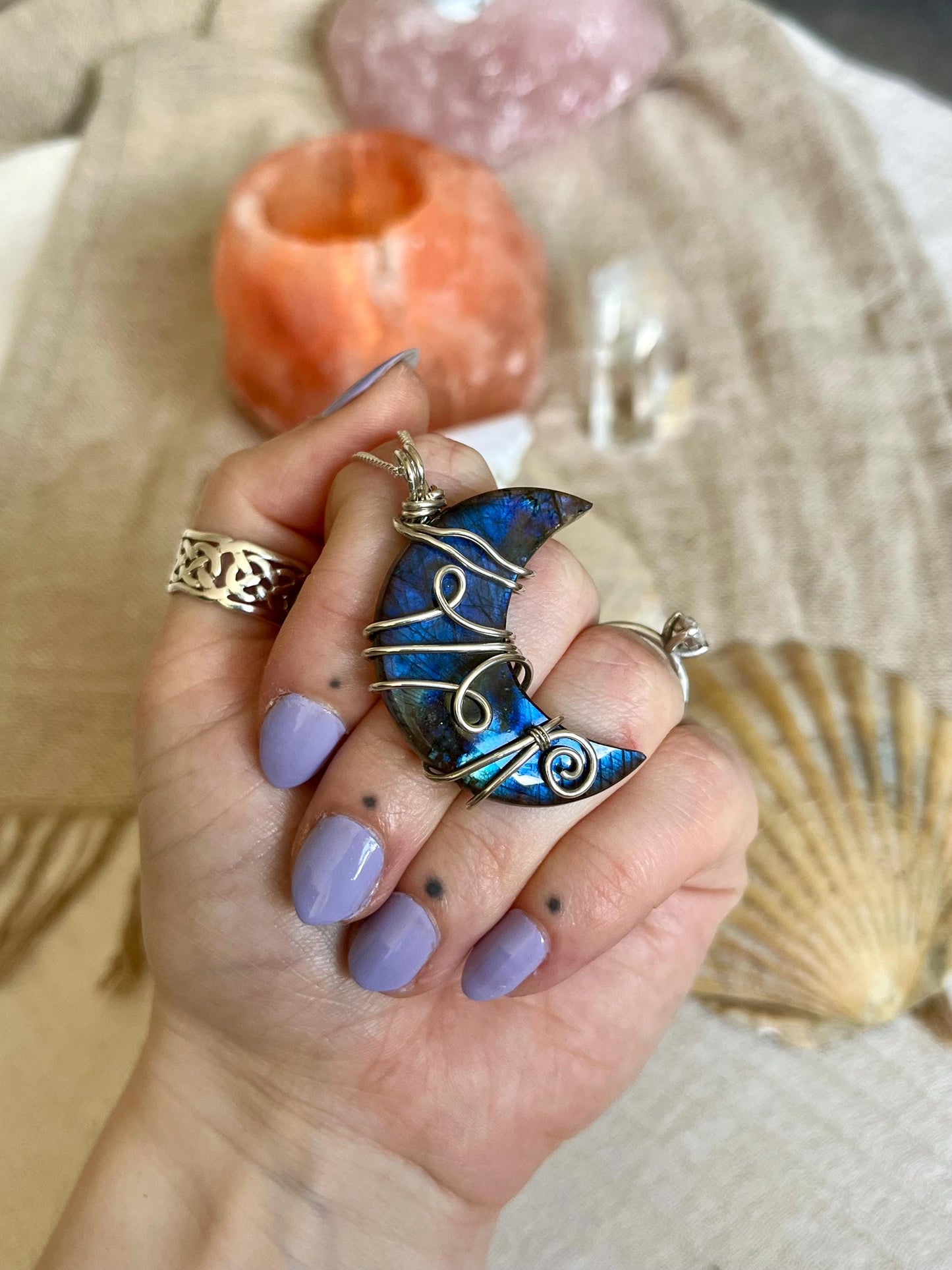Hand holding a blue and silver pendant with a shell and crystal in the background
