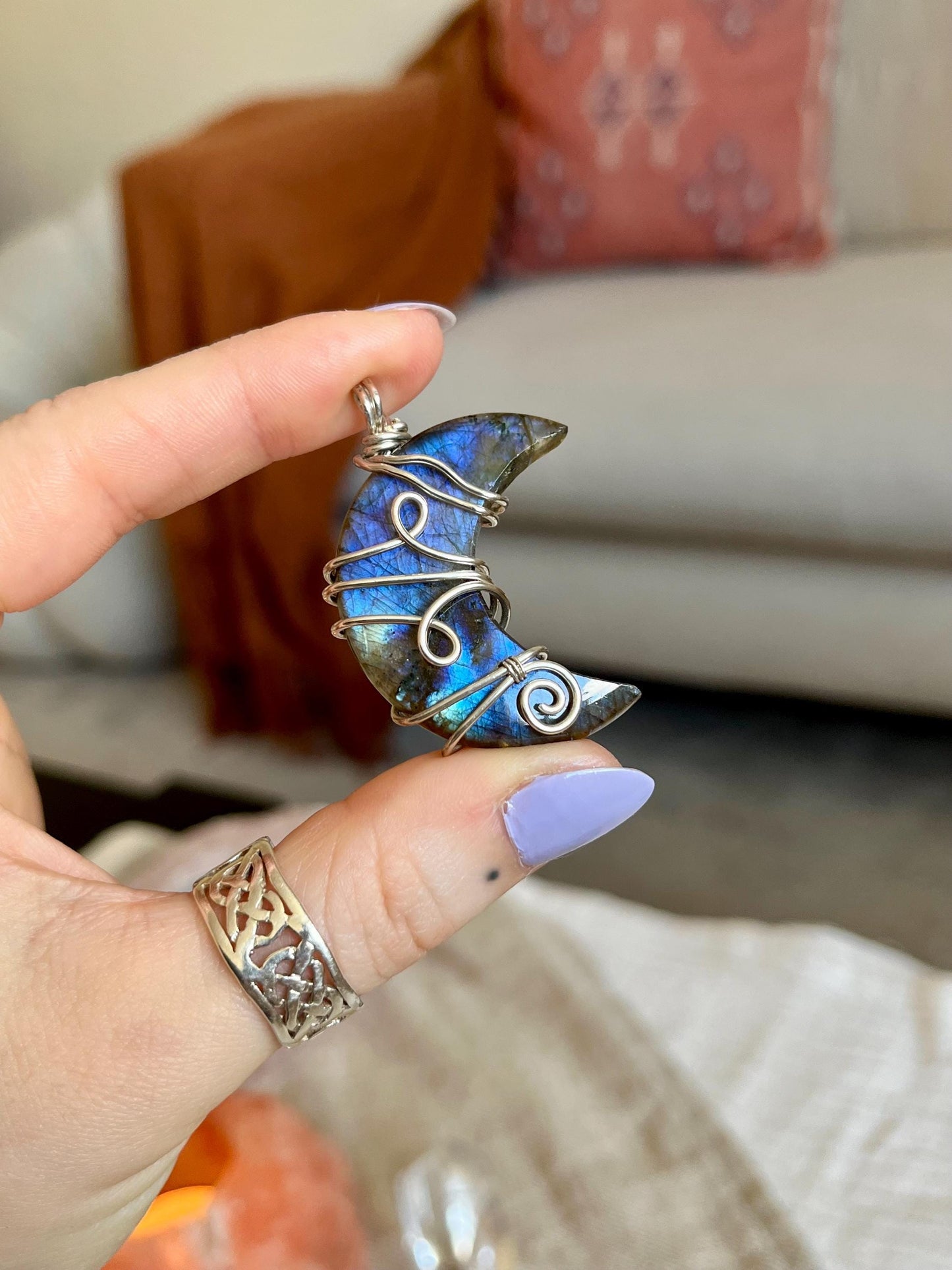 Hand holding a blue stone pendant with silver wire wrapping against a blurred indoor background Labradorite