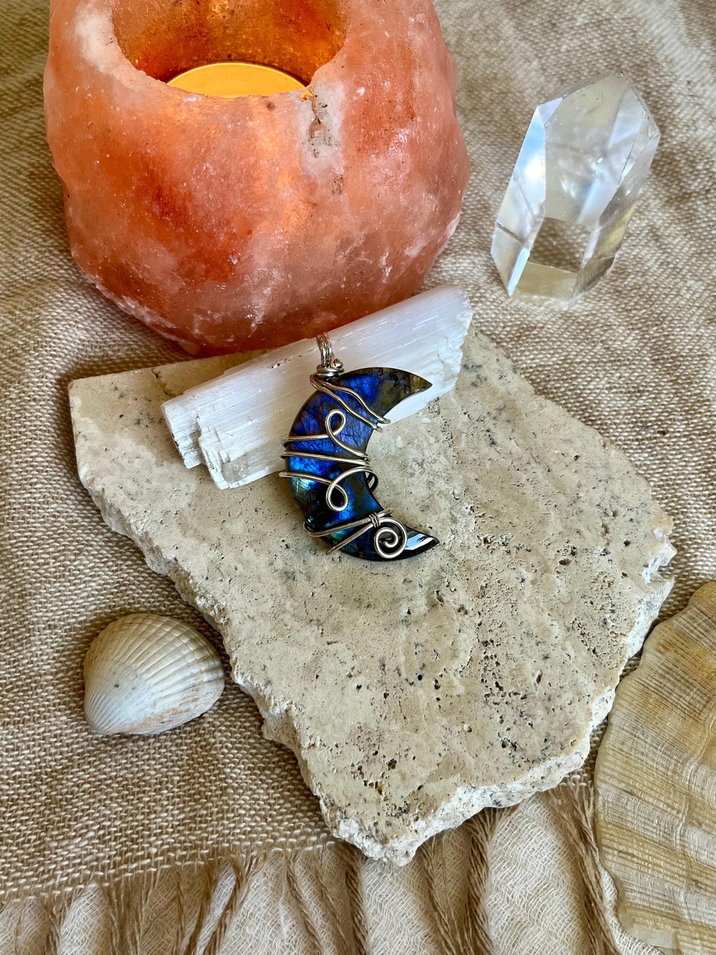 Decorative stone Labradorite 
with a moon-shaped pendant, crystal, and shell on a textured surface