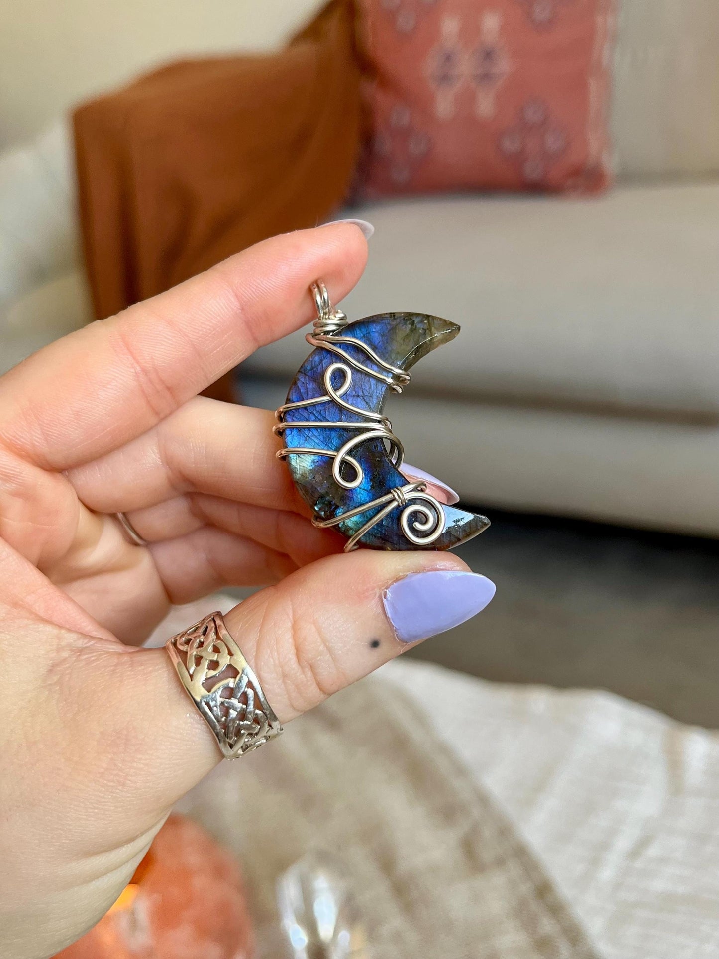 Hand holding a blue and silver pendant with a blurred indoor background