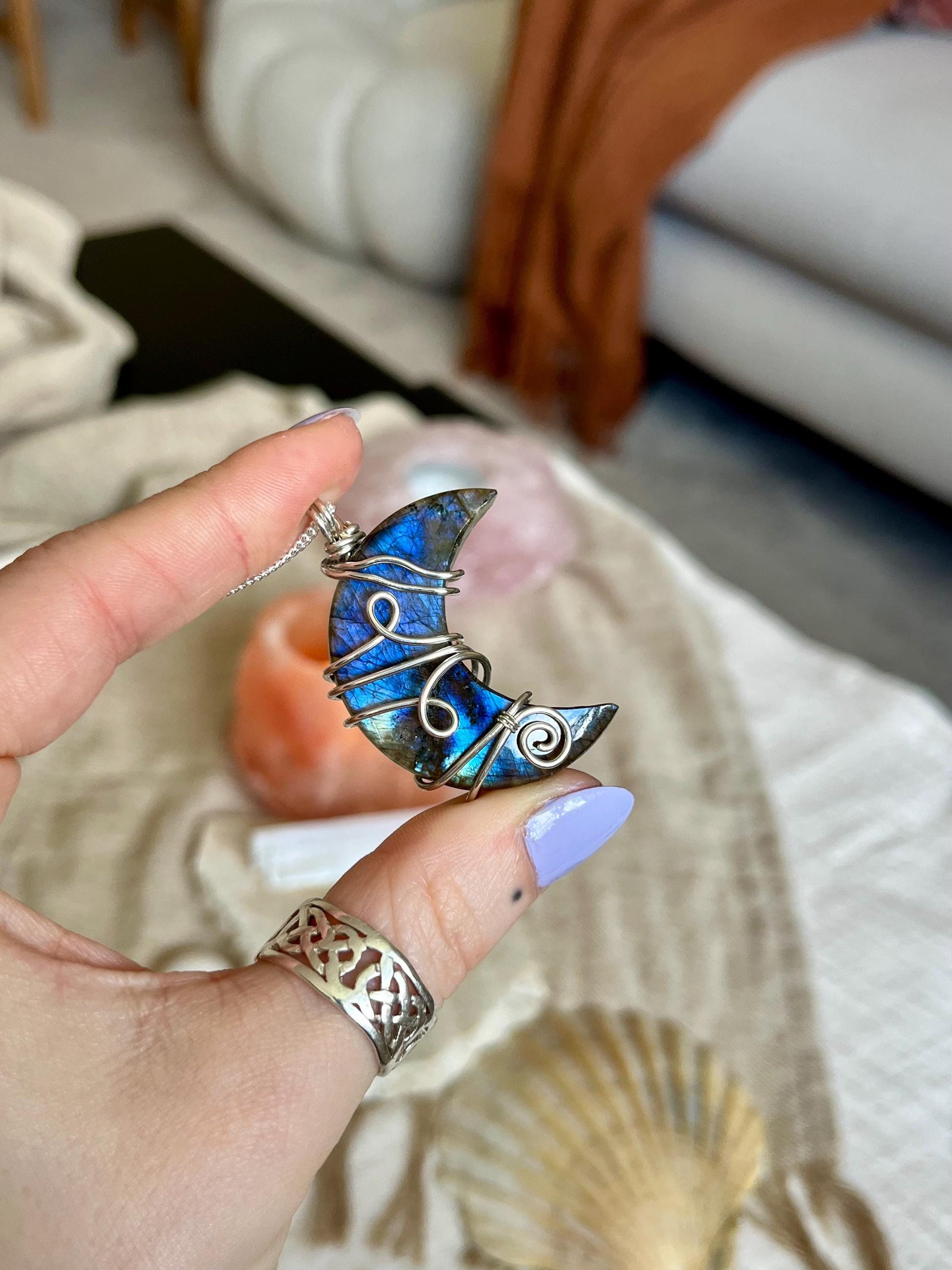 Hand holding a blue and silver crescent moon-shaped pendant with a blurred indoor background.